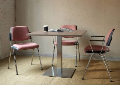 Three stackable meeting chairs with soft cushion seat and back pads, chrome legs and optional arm rests around a square wood effect table with metal base