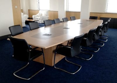 Large bespoke barrel shape boardroom table in wood veneer with integrated cable management, black leather and chrome meeting chairs, armchairs and coffee table