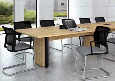 Boardroom chairs with grey fabric seats, black mesh backs and chrome frames around a large wood effect and black barrel shaped boardroom table