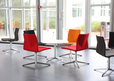 Red, orange and brown fabric occasional chairs with metal legs and matching circular table with a white top