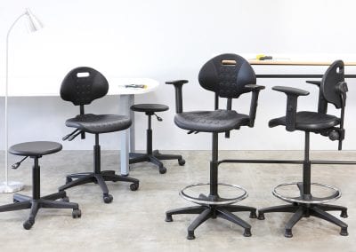 A selection of adjustable operator task stools with wheeled or fixed bases, back rests, foot rests and arms, white meeting table and high bench table