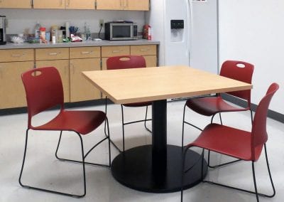 Square wood effect table with heavy black base and red plastic and black wireframe stackable chairs