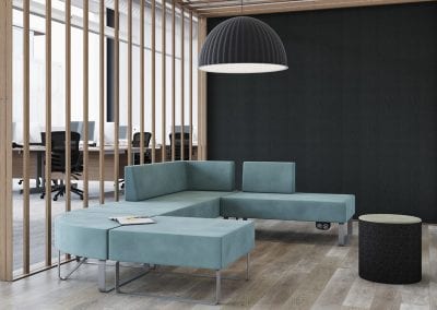 Modular designer sofa with grey metal legs and integrated under seat power ports with mesh back operator task chairs and beam desks in the background