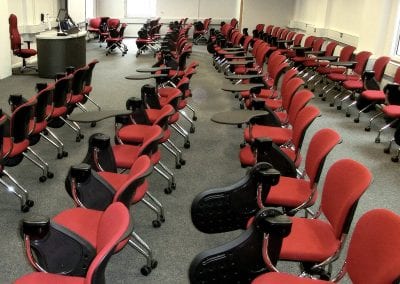 Meeting room with rows of functional meeting chairs with integrated folding writing tables, presentation pod and fully adjustable operators chair