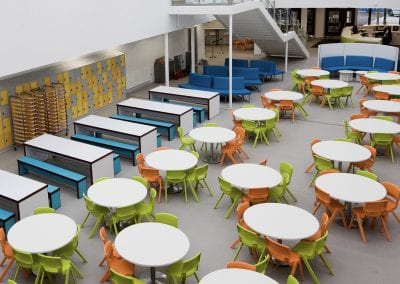 Large dining refectory with white top circular and bench tables with plastic stacking chairs and bench seating. Personal effects lockers and modular curved sofa seating