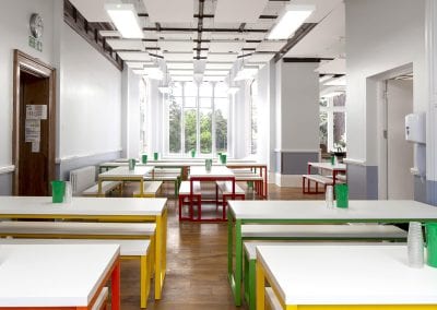 White top bench tables with coloured metal frame legs with matching bench seats in a dining refectory room