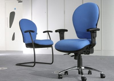 Two teacher chairs, both with blue fabric. One in fixed leg meeting style with arm rests and one in fully adjustable operator style with swivel castor base and arm rests
