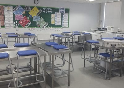 Science lab or catering kitchen stools with blue plastic seats and metal frames with hygenic steel work benches