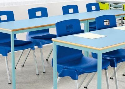 Classroom tables with colour tops and frame options, shown with blue molded stacking chairs and tray storage units