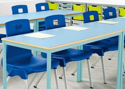 Classroom tables with colour tops and frame options, shown with blue molded stacking chairs and tray storage units