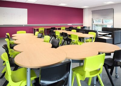 Staff room modular meeting and dining tables with wood effect tops, grey metal legs, lime green and black stackable plastic chairs and black leather modular sofa seating