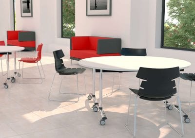 Circular tilt top tables with chrome legs on castors with red and black formed meeting chairs and matching colour sofas