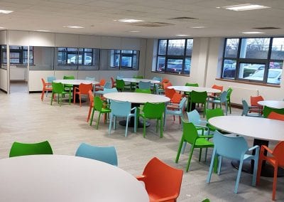 White circular canteen table with heavy duty centre leg, surrounded by coloured plastic stacking chairs