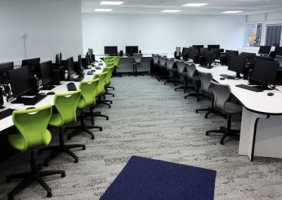 Large educational computer rooms with custom fitted white top tables and swivel base operator chairs