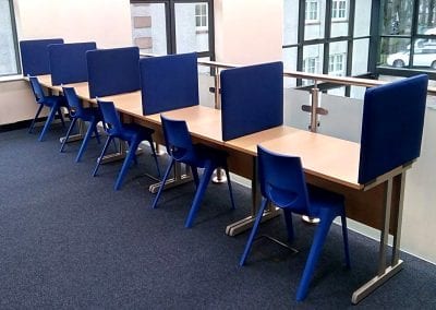 Educational library study desks with blue divider screens and blue stacking chairs