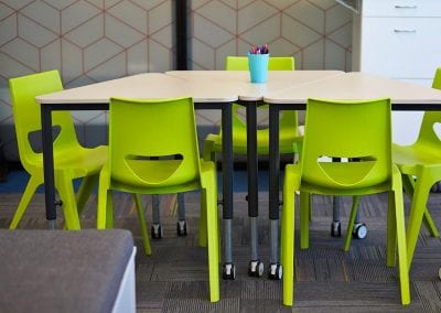 Triangular modular educational tables on castors with wood veneer tops and black legs, and lime green plastic stacking chairs