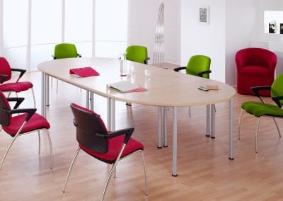 Modular Elite office tables shown here with the half round tables at each end to form an oval meeting table surrounded by red and green fabric covered meeting chairs