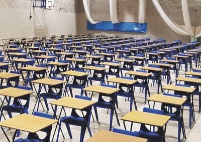 Folding educational exam tables with wooden tops, metal legs and pen groove, and blue plastic stacking chairs