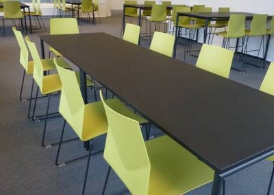 All black rectangular dining tables with metal legs surrounded by lime green angular dining chairs with black legs