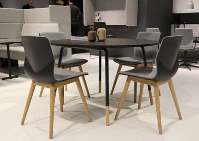 Black topped circular meeting table with wooden leg highlights and contrasting meeting chairs