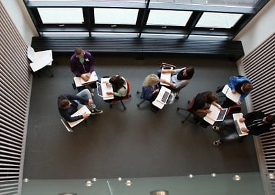 Photograph looking down on students sitting on wheeled meeting chairs in various colours