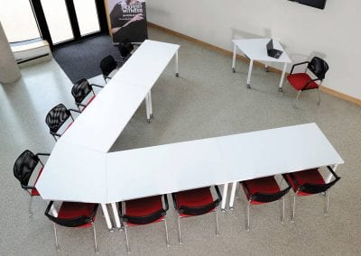 Modular white meeting tables formed in an arrow configuration with red and black meeting chairs