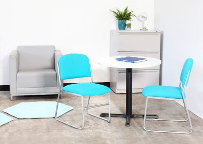 Staff room circular white table with black metal base, two stacking metal framed chairs, 3 drawer filing cabinet and occasional grey tub chair