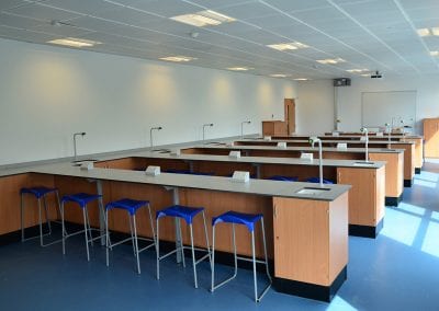 Science lab with fully integrated work stations, wash stands, electric sockets and blue seat stools with metal legs