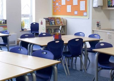 Classroom with wood veneer tables, blue molded plastic stacking chairs and wheeled book display stand