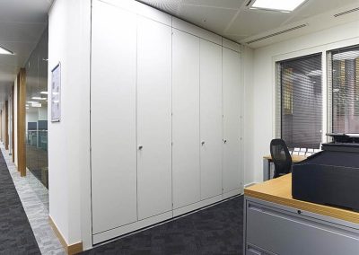 Built in floor to ceiling white finish wall storage units with double doors forming an integral part of the office layout