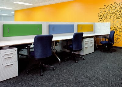 Coloured desk divider acoustic panels attached to desktop screens in an open plan office environment