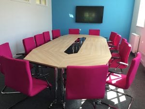 Modular conference table with wood veneer tops and chrome legs, surrounded by pink fabric meeting chairs with chrome frames