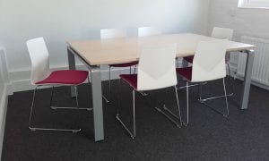 Formed white meeting chairs with padded seats and chrome legs around a veneer meeting table with chunky grey legs